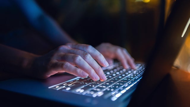 Close up of woman's hand typing on computer keyboard in the dark, working late on laptop at home 