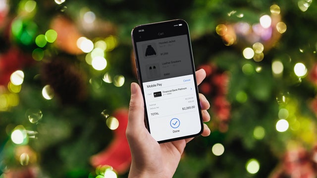 Female hand doing Christmas shopping online with smartphone, making mobile payment with credit card against illuminated Christmas tree with fairy lights. Christmas theme. Christmas shopping. Christmas sale. Contactless payment. Lifestyle and technology 