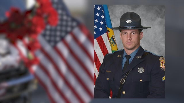 A photo of Corporal Matthew Snook in the foreground, a flag and flowers in the background 