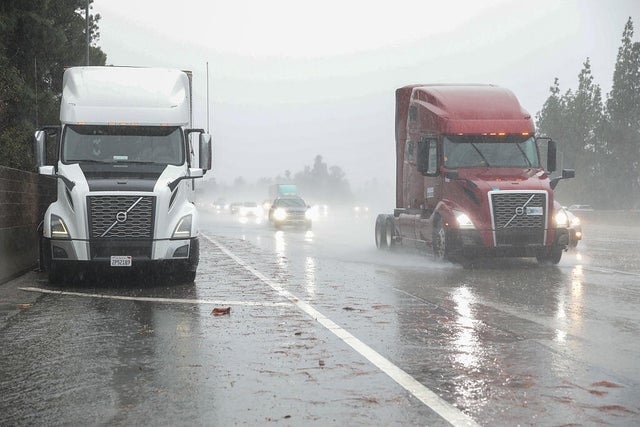 A person in a safety vest standing in water as he rakes leaves 