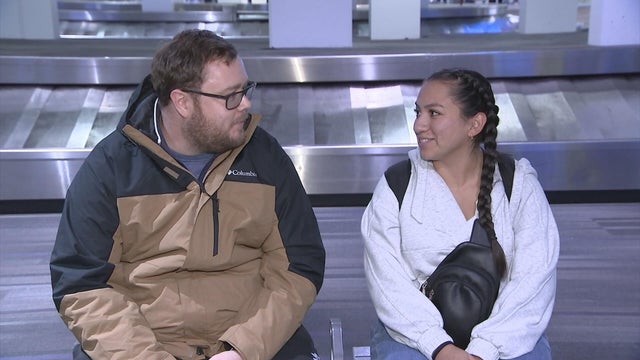 Two travelers at PHL sit near a baggage claim carousel 