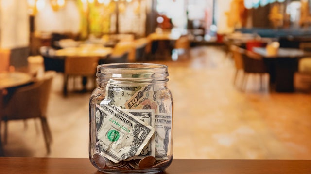 Tip jar in restaurant dining room. Service industry tipping, minimum wage and gratuity concept. 