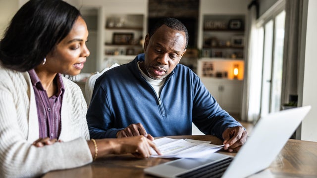 Husband and wife looking over bills and using laptop in domestic kitchen 