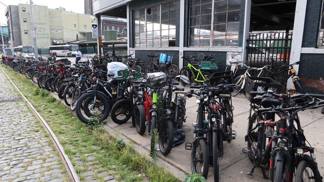 Dozens of e-bikes used by restaurant delivery workers lined up outside the Hoboken transit terminal in 2024 