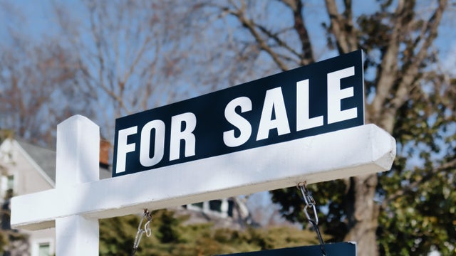 For Sale Sign Hangs in Front Yard of House 
