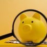 Yellow piggy bank with magnifying glass and puzzles. Financial planning and investment strategy concept. 
