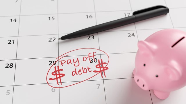 A pink piggy bank, a pen and a calendar marked with the word pay off debt and dollar signs in red on a date. Illustration of the concept of financial debt, loans and owing money 
