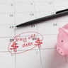 A pink piggy bank, a pen and a calendar marked with the word pay off debt and dollar signs in red on a date. Illustration of the concept of financial debt, loans and owing money 