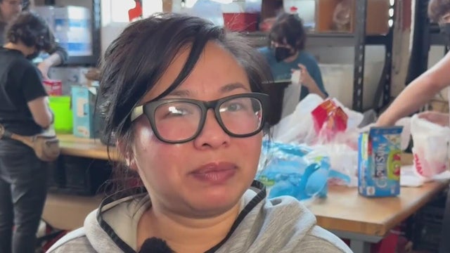 Woman wearing glasses stands in front of volunteers packing food into grocery bags 