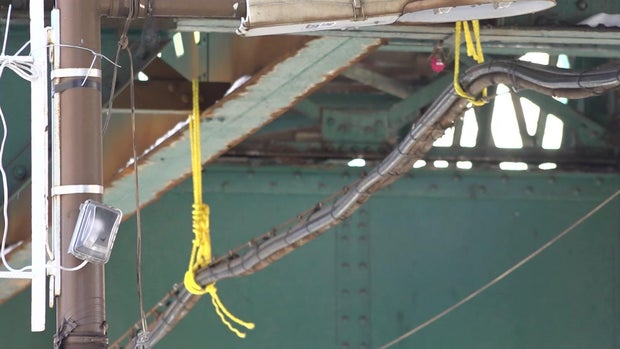 Communication cables hang by yellow cords from elevated subway tracks 