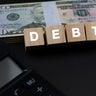 Debt Text On Wood Block With US Paper Currency and Calculator 