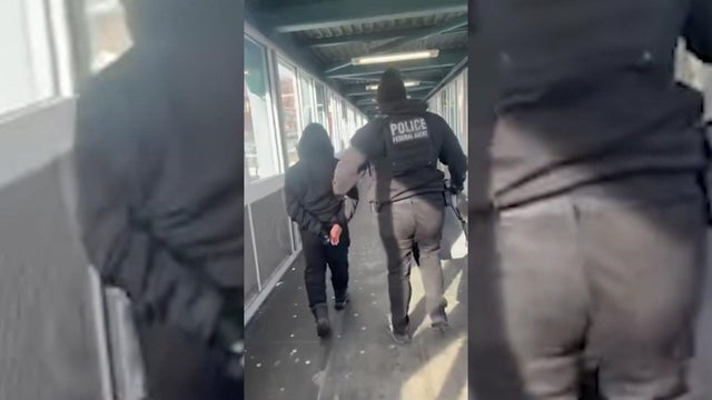 An ICE agent walking with a man in handcuffs at a Jersey City light rail station 
