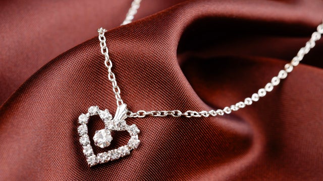 Heart-shaped pendant with silver necklace on brown silk background, Symbols of love concept. 