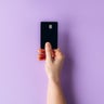 Female hand holding a black credit card against a pastel purple background for payment or finance concept 
