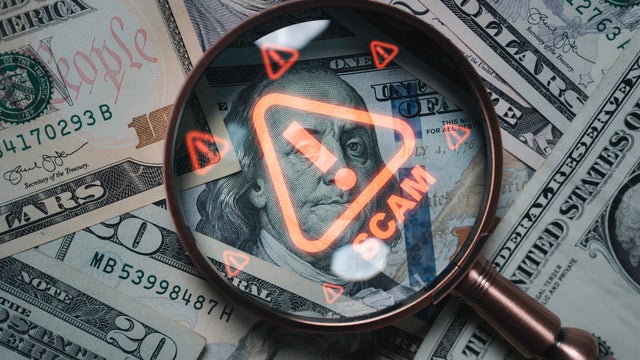 Magnifying glass focusing on scam warning symbol over dollar bills concept of financial fraud money laundering cybercrime and online scam alert for security awareness and finance protection 