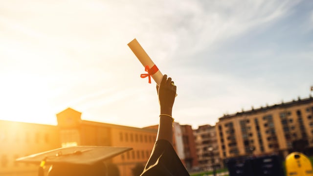 Young black student holds up graduation diploma at sunset 