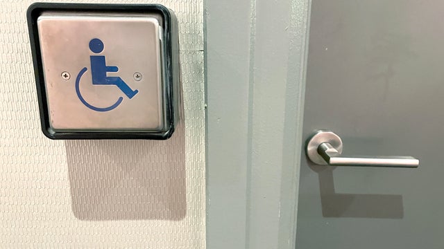 A silver button with a wheelchair logo on a wall next to a door 