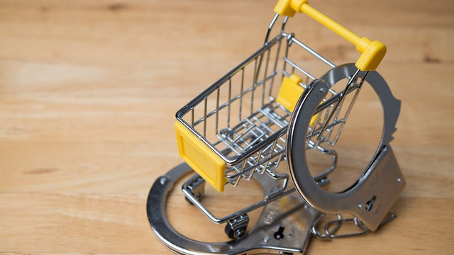 Handcuffs locked shopping cart on wooden table background copy space. 