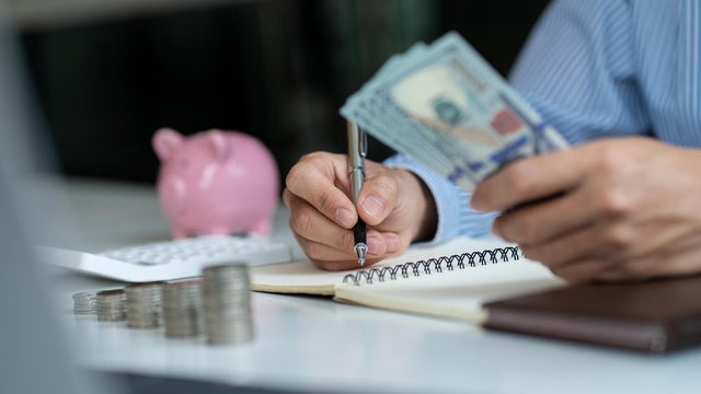 man holding a dollar bill use money calculator Keep a record of the amount of money he accumulates throughout the year with piles of coins and piggy banks for future business investments. 