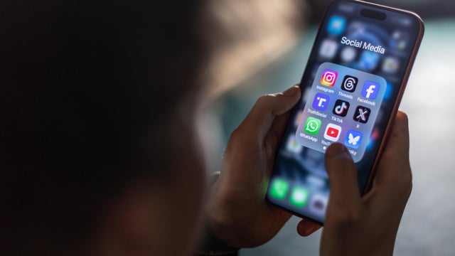 A teen holds an iPhone displaying social media and messaging apps on the screen 
