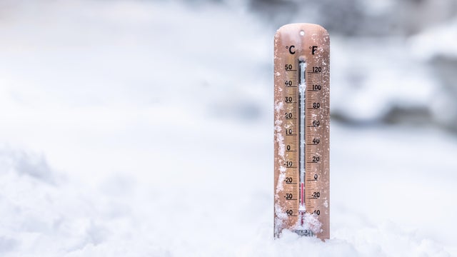 A copper thermometer stuck directly into deep snow, clearly displaying both Celsius and Fahrenheit scales. The red bar shows a freezing temperature of approximately -20&deg;C (equivalent to roughly -4&deg;F) 