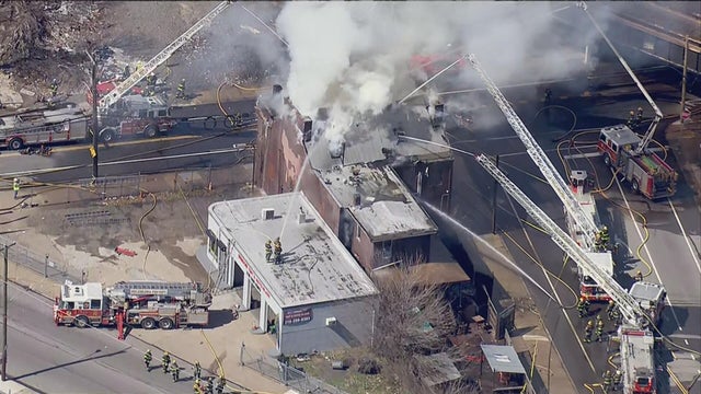 Firetrucks are on the scene, shooting water onto a fire at a brick building, smoke is coming from the building 