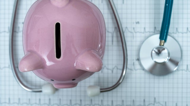 Piggy bank with stethoscope on illustration of wave form on checked ecg graph background, health saving account, insurance, top view 