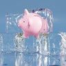 Pink piggy bank partially in an ice cube on blue background. Illustration of the concept of confiscated and impounded illegal assets, frozen assets and economic stagnation 
