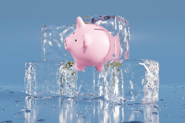 Pink piggy bank partially in an ice cube on blue background. Illustration of the concept of confiscated and impounded illegal assets, frozen assets and economic stagnation