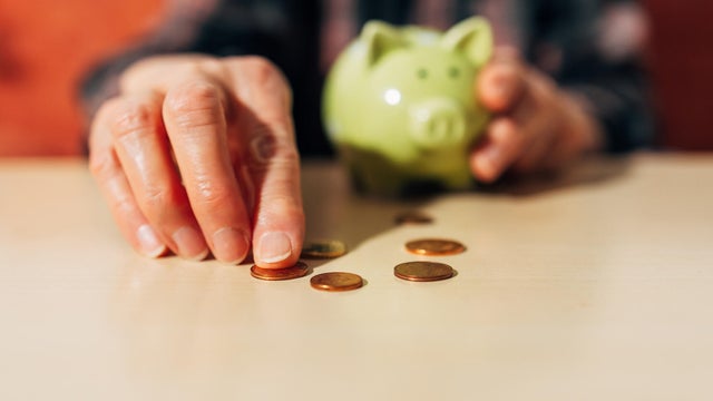 senior women Hand collecting coins on a table with a piggy bank in the background 