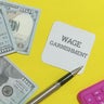 Wage garnishment documents with money and calculator on yellow background 