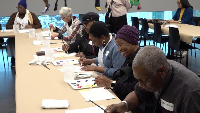 People painting on pieces of paper at a table 