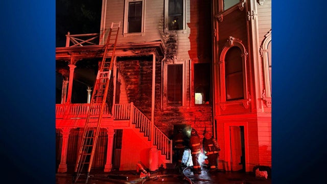 Firefighters near a Victorian mansion that has a scorched exterior 