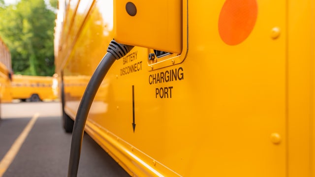 Yellow electric school bus plugged in at a charging station. 