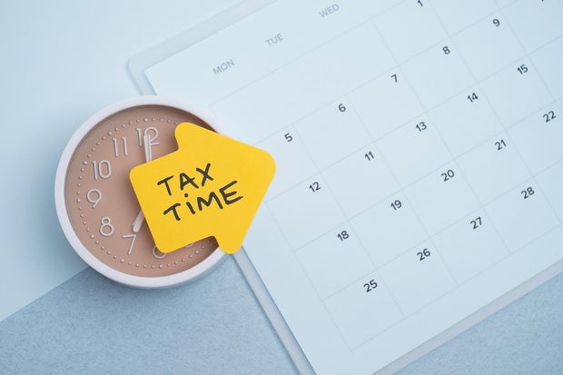 Tax time concept. Reminder sticker on clock and calendar background 