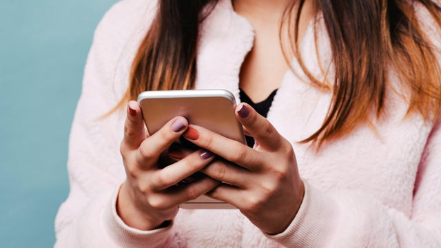 Teen Female Texting on a Smart Phone with Solid Blue Background and Pink Fur Jacket 