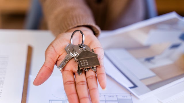 Person holding new house keys and home plans 