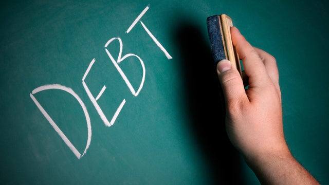 Hand preparing to erase the word DEBT from a chalkboard 