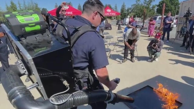 a person with a backpack holds a device that uses soundwaves to put out fires 