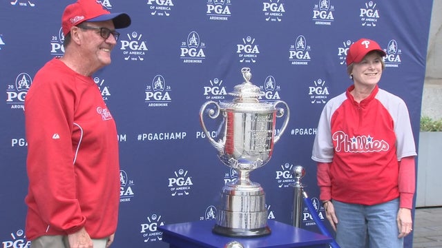 A man and woman wearing Phillies gear smile for a photo with the PGA Championship trophy 