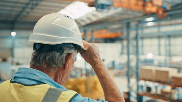 A senior or old warehouse or factory worker looking out at the stock in a cargo plant due for delivery or shipping. Mature male storehouse or supply chain manager working in the logistics industry 