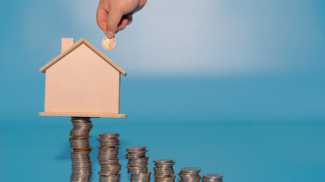 Hand inserting coin into house model on top of coins stacks. Save and investment money concept. 