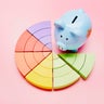 High angle view of a piggy bank and colorful pie chart on pink background 