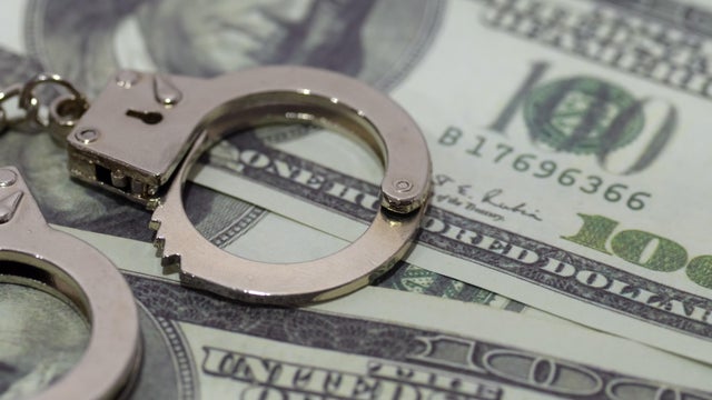 a pair of handcuffs lying on a bed of U.S. dollar bills. This juxtaposition suggests the corrupting influence of money or the potential for financial crimes. 