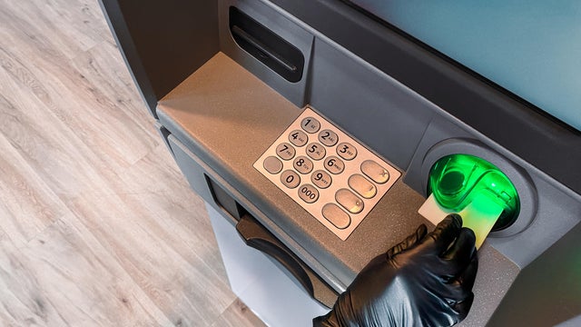 Gloved hand inserting card into ATM machine 