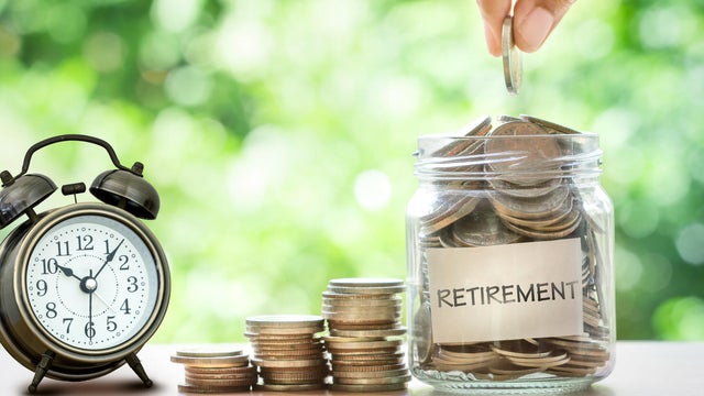 Hand putting Coins in glass jar with retro alarm clock 