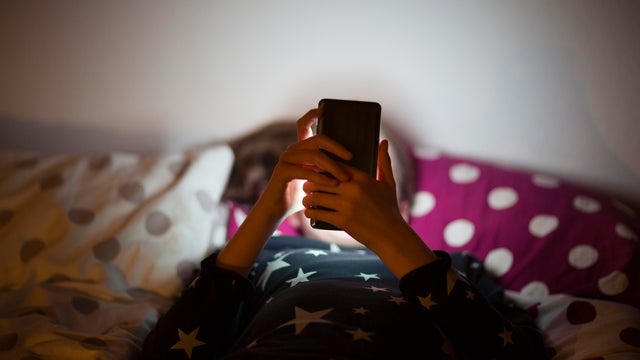 Girl lying on bed at night and using a mobile phone 