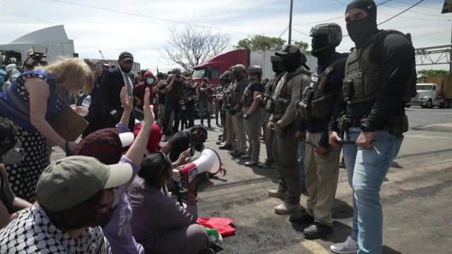 Protesters sit on the ground in front of a line of ICE agents 
