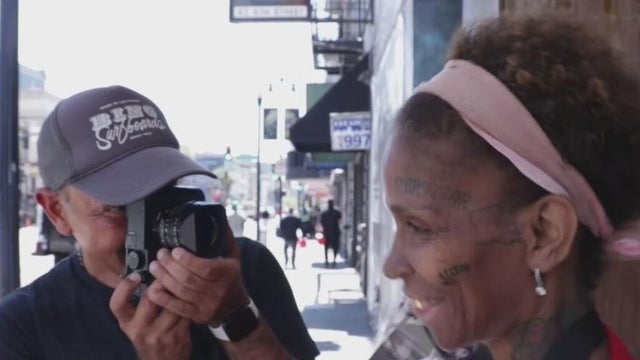 A photographer takes a portrait of a woman who is holding up several photographs 