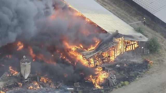 a burning structure with a firefighter nearby hosing it with water 